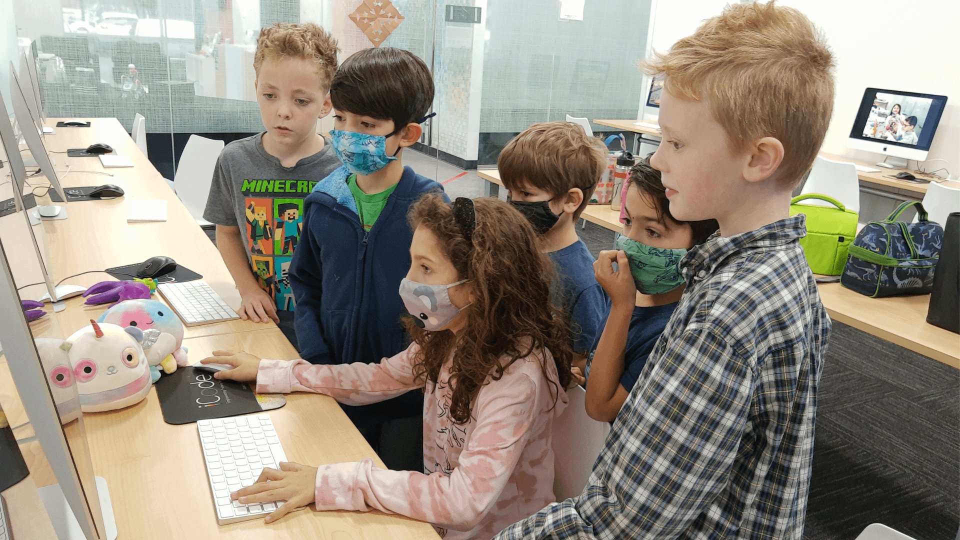 Kids Coding - a girl kid is practicing a coding in iCode school inside the classroom while other students are watching her computer